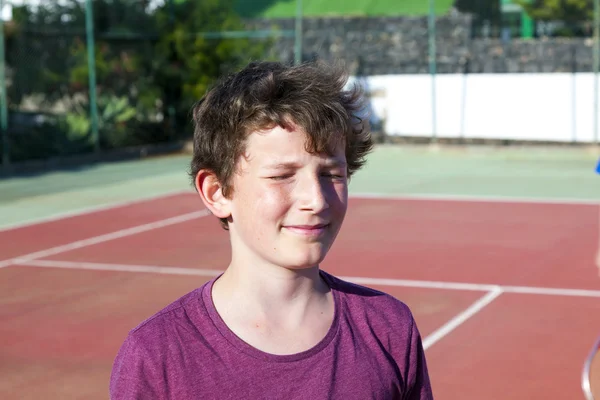 Niño sonriente inteligente en la cancha de tenis al aire libre con los ojos cerrados —  Fotos de Stock