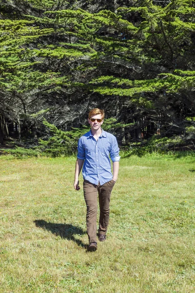 Teenage boy with sunglasses walks happy on the meadow — Stock Photo, Image