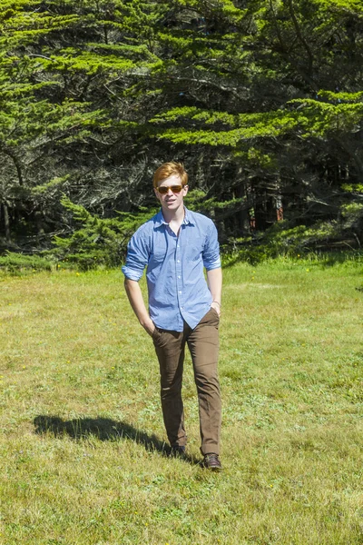 Teenage boy with sunglasses walks happy on the meadow — Stock Photo, Image