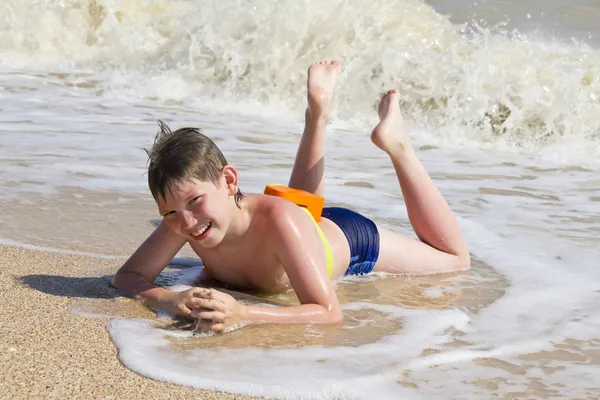 Kluk leží na pláži v příboji — Stock fotografie