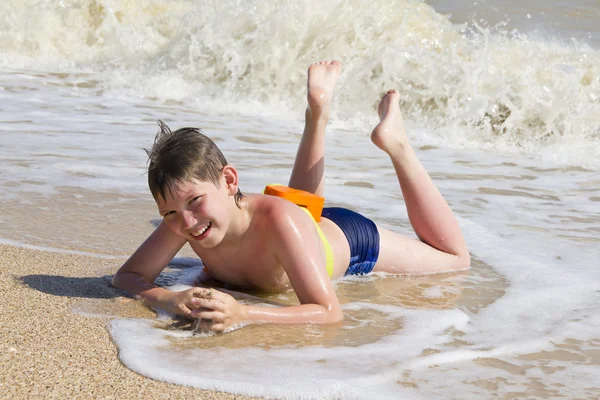 Kluk leží na pláži v příboji Stock Fotografie