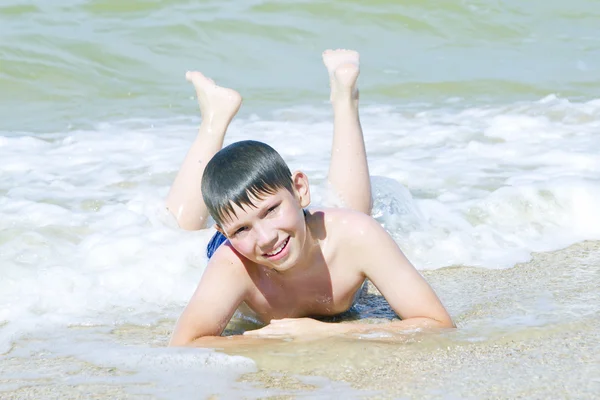 Niño acostado en la playa en el oleaje —  Fotos de Stock