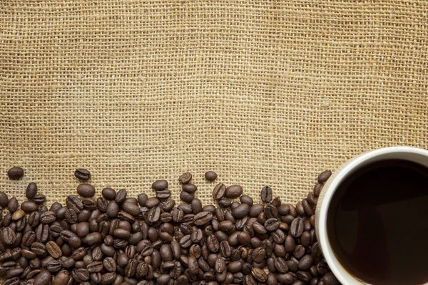 Granos de café y taza sobre arpillera — Foto de Stock