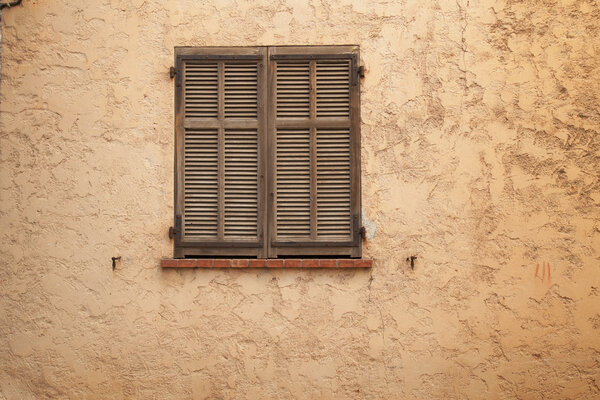 Old and and weathered closed shutters and weathered stucco wall.