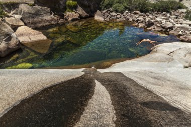 Young woman dives into a prestine mountain pool. clipart