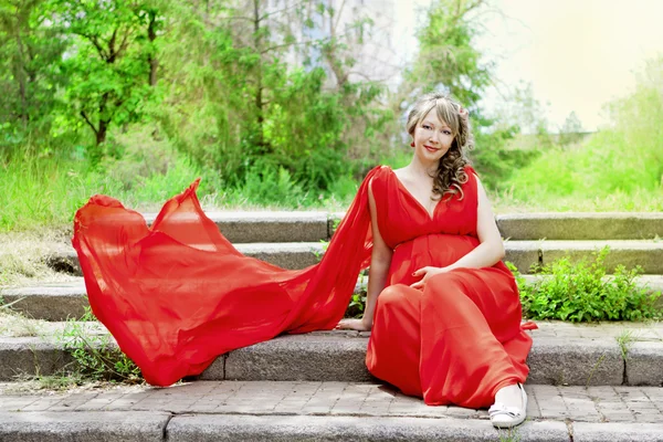 Zwangere vrouw in rode jurk zit — Stockfoto