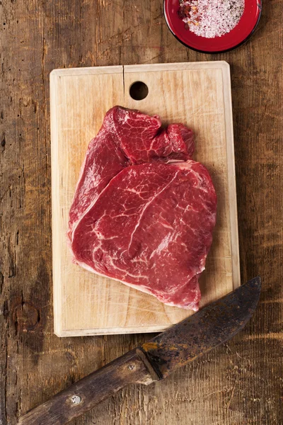 Bife cru de carne de caçarola com faca na mesa de madeira — Fotografia de Stock