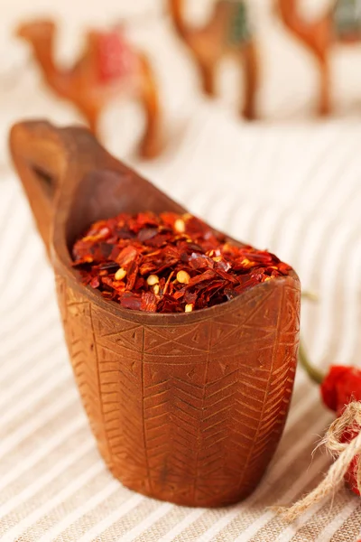 Fiocchi di carta peperoncino rosso in ciotola di legno curvato e carava di cammello — Foto Stock