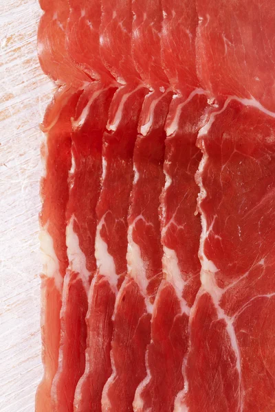Dry cured ham slices on white wood background — Stock Photo, Image