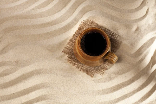 Black coffee in mug on beach sand background, top view — Stock Photo, Image