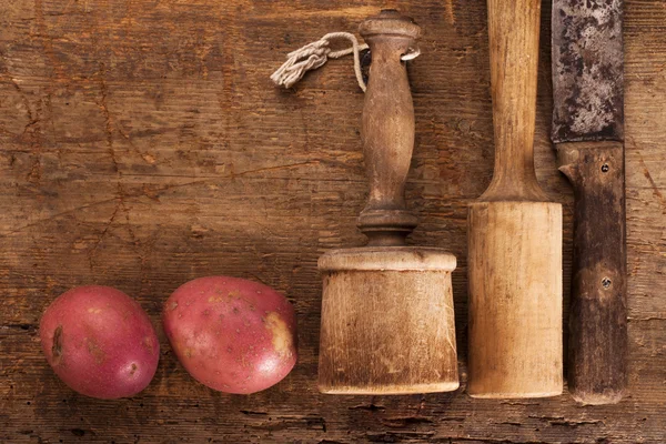 Antikke kartoffelmashers og kniv på gammelt træbord med rødt - Stock-foto
