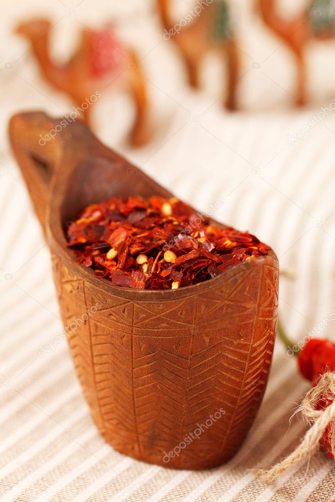 Red chillies paper flakes in curved wooden bowl and camel carava