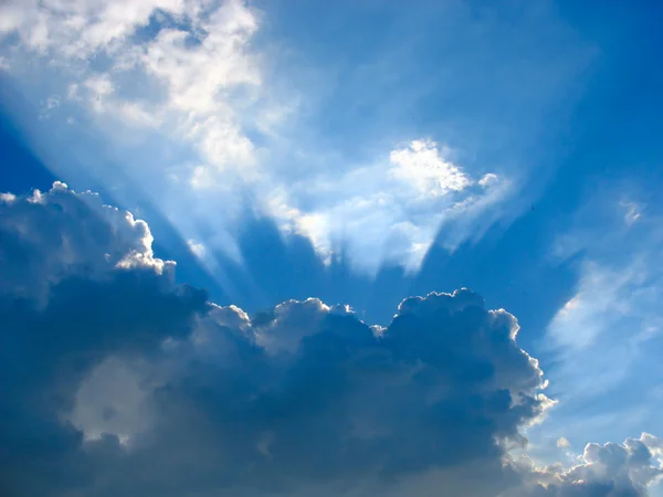 Blauwe lucht met stralen van de zon door de wolken — Stockfoto