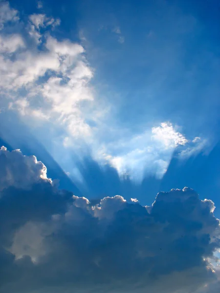 Голубое небо с солнечными лучами сквозь облака — стоковое фото