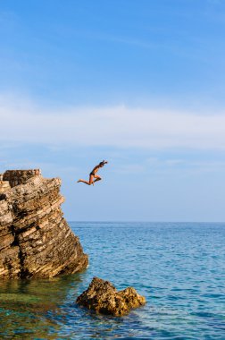 Boy Jumping Off Cliff Into Blue Water clipart