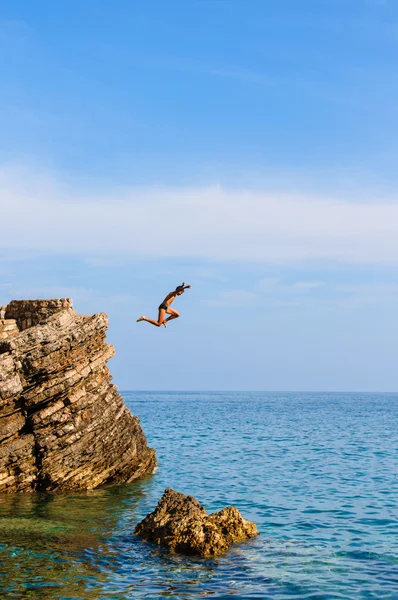 Junge springt von Klippe ins blaue Wasser — Stockfoto