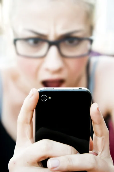 Шокированная блондинка смотрит на свой смартфон — стоковое фото