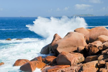 Sea wave breaks against the pink granite rocks clipart