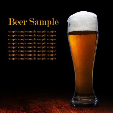 Beer into glass on a black and wooden table clipart