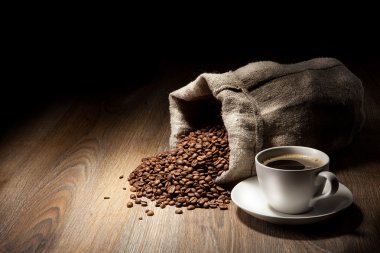 Coffee cup with burlap sack of roasted beans on rustic table clipart