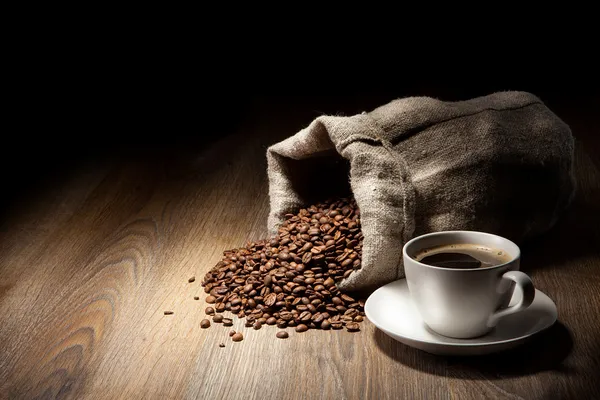 素朴なテーブルに焙煎した豆の黄麻布の袋のコーヒー カップ — ストック写真