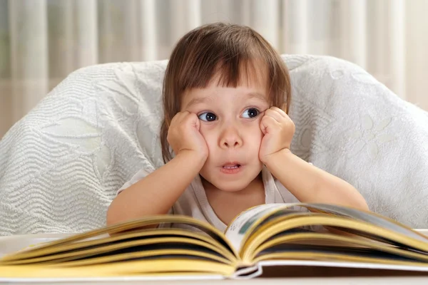 Маленькая белая девочка сидит за столом с книгой — стоковое фото