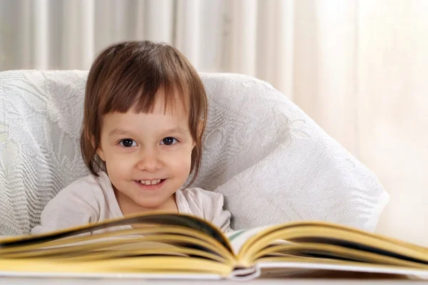 Pequena criança branca sentada em uma mesa com um livro — Fotografia de Stock