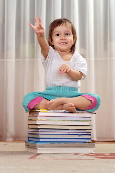 Little Caucasian nice girl sitting on a pile of books — Stock Photo, Image