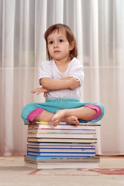 Pequeña caucásica buena chica sentada en un montón de libros —  Fotos de Stock