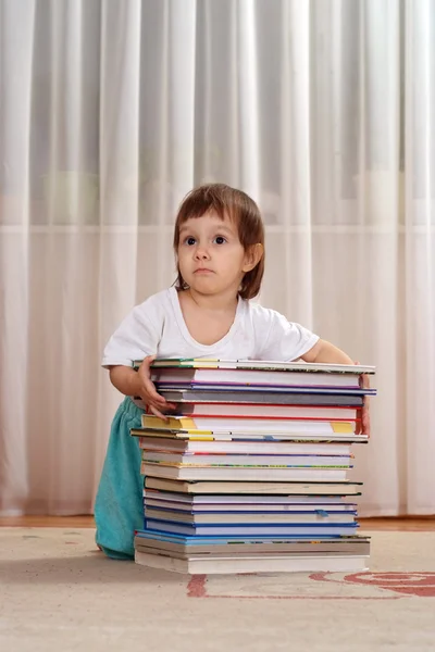 Lilla kaukasiska flicka sitter bakom en trave böcker — Stockfoto