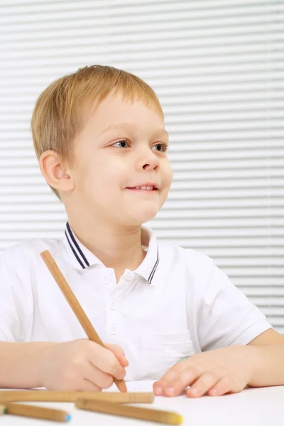 Маленький хлопчик сидить за столом з олівцем — стокове фото