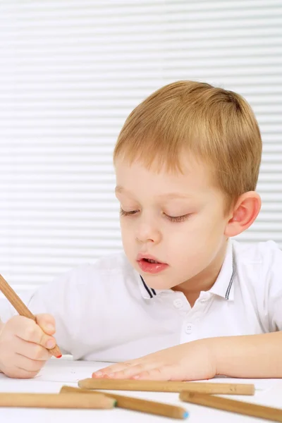 Маленький хлопчик сидить за столом з олівцем — стокове фото
