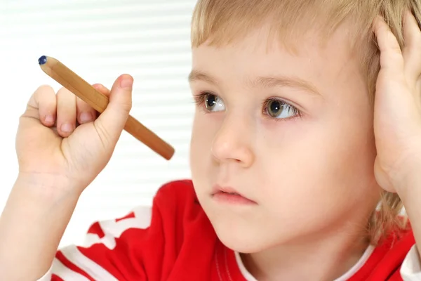Un niño sentado en una mesa con un lápiz — Foto de Stock