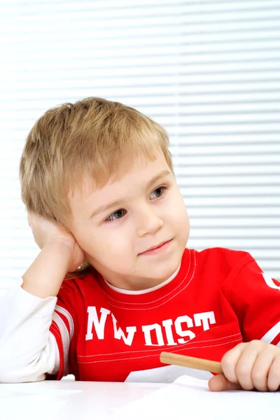 A youngster sitting at a table with a pencil — Stock Photo, Image