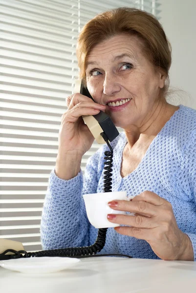Mujer mayor caucásica con una taza y un teléfono — Foto de Stock