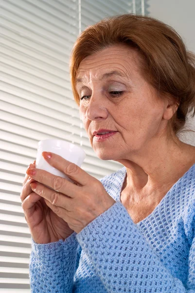 An elderly woman looks at a cup — Stock Photo, Image