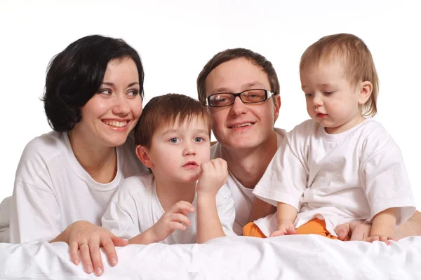 Een gelukkige familie van vier in de witte shirts op een bed — Stockfoto