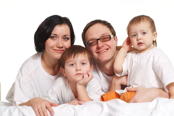 Родители с детьми в белых рубашках на кровати — стоковое фото