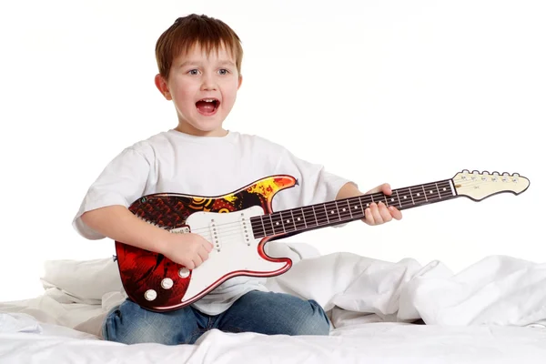 A boy with a guitar sitting on a bed — Stock Photo, Image