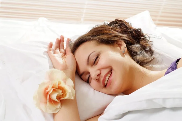 A beautiful caucasian happy girl with a flower in a bed — Stock Photo, Image