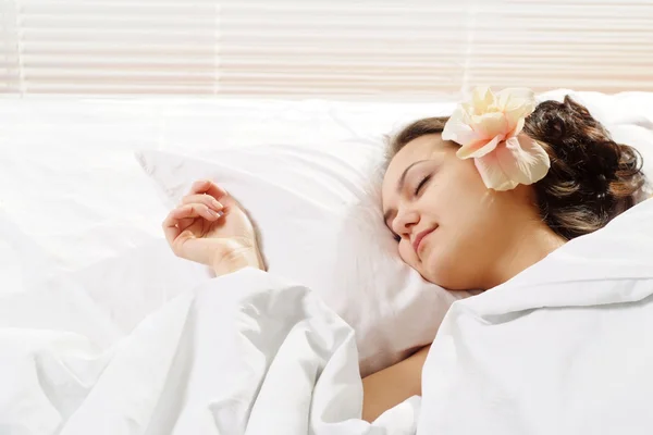 A beautiful caucasian joy girl with a flower in a bed — Stock Photo, Image