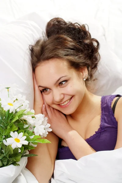 Güzel beyaz bir gülümseme kız yatakta bir buket çiçek — Stok fotoğraf