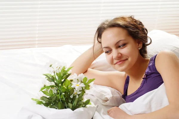 Een mooie Kaukasische vrouw in bed met een boeket van bloemen — Stockfoto