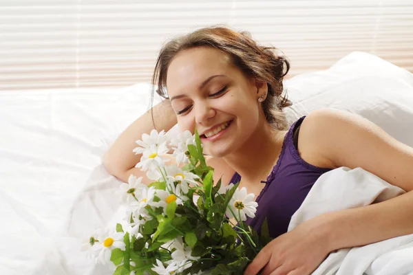 Una hermosa hembra caucásica en la cama con un ramo de flores — Foto de Stock