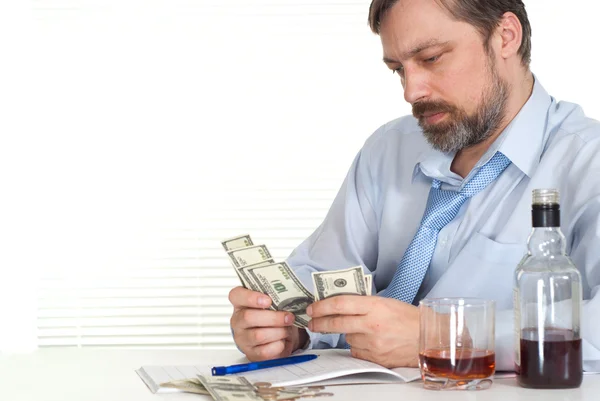 Businessman sitting at a table with a bottle and money — Stock Photo, Image