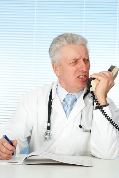 Felice medico caucasico con un telefono seduto — Foto Stock