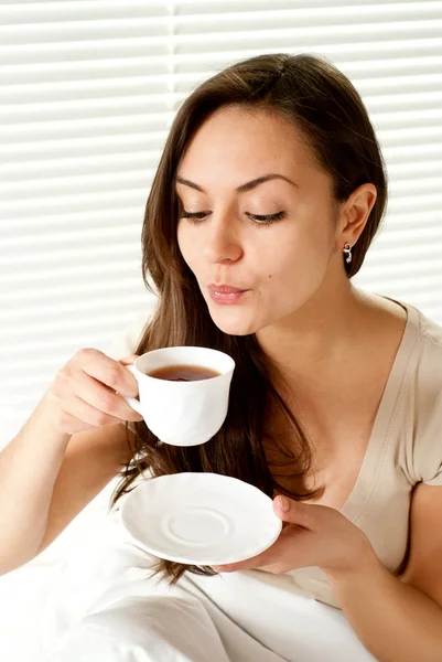 Mulher branca jovem sentada com uma xícara na cama — Fotografia de Stock