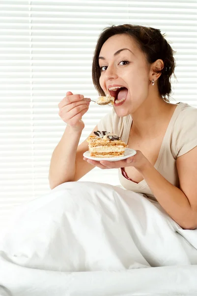 Junge kaukasische Frau sitzt im Bett mit einem Kuchen — Stockfoto