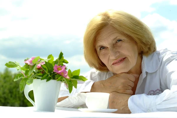 Vakker, hvit, eldre kvinne som sitter med en blomst – stockfoto