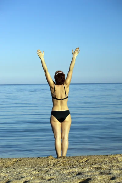 Гармоничная девушка стоит у моря, подняв руки — стоковое фото